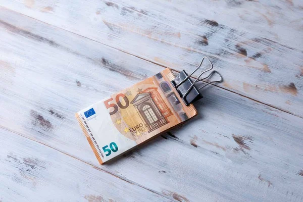 money bundle, 50 euro notes held with a rusty foldback or blinder clip, isolated on a wooden table