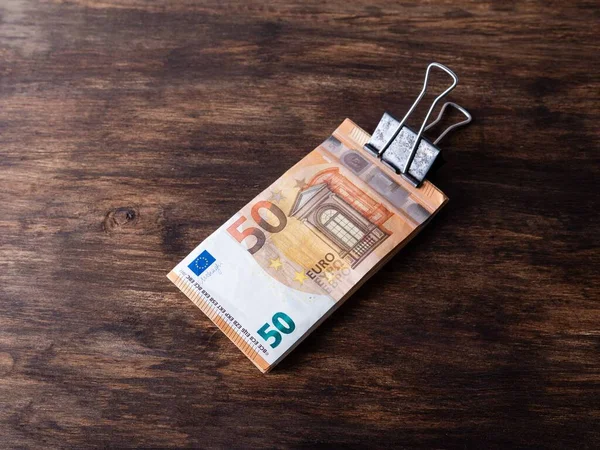 bundle of 50 euro notes held with a rusty binder clip, isolated on dark wooden background