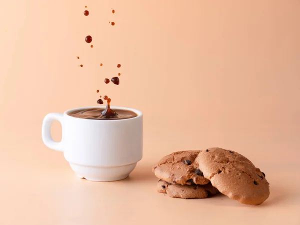 drops of coffee falling on a cup of coffee, three biscuits, all isolated on a light background, breakfast concept