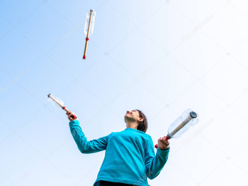 young girl playing in the garden, juggling with home made juggling clubs, isolated outdoors, active lifestyle and sports concept