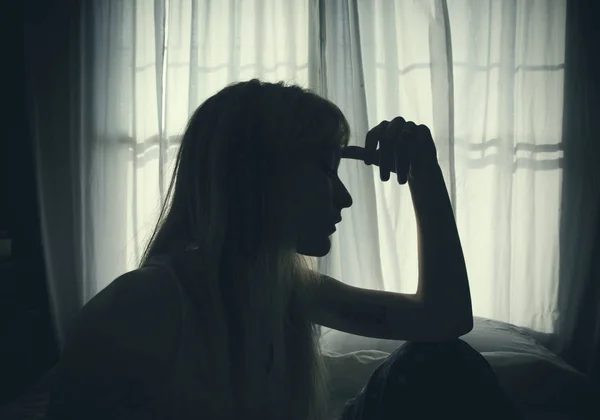 Silhouette of woman sitting in bed by window — Stock Photo, Image