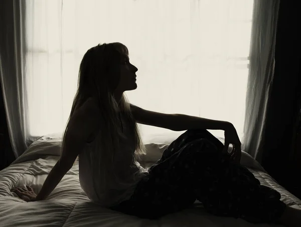 Silueta de mujer sentada en la cama por la ventana — Foto de Stock