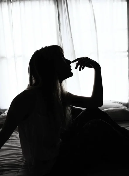 Silhueta de mulher sentada na cama pela janela — Fotografia de Stock