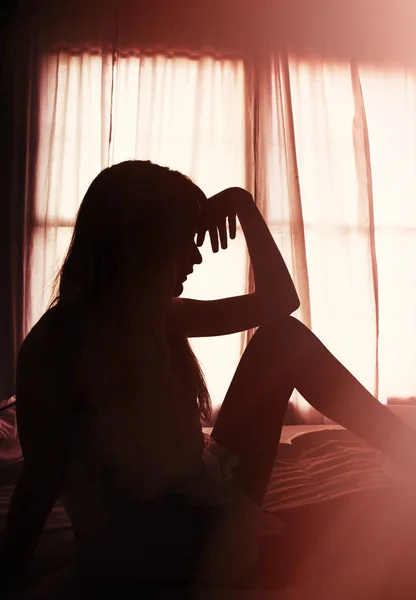 Silueta de mujer sentada en la cama por la ventana en la luz de la mañana — Foto de Stock