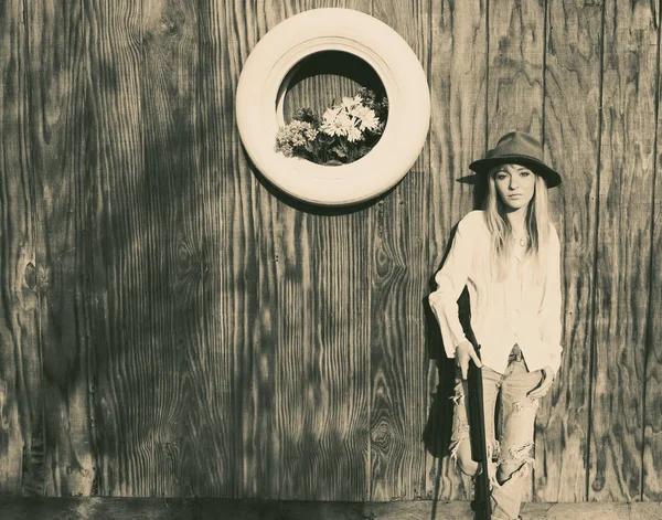 Femme avec pistolet appuyé contre un mur en bois avec pneu blanc avec des fleurs . — Photo