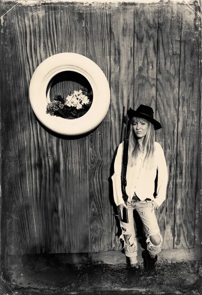 Femme avec pistolet appuyé contre un mur en bois avec pneu blanc avec des fleurs . — Photo