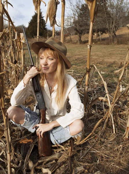Mulher bonita sentada no campo de milho com uma arma — Fotografia de Stock