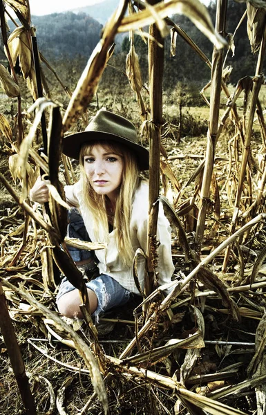 Красивая женщина сидит на кукурузном поле с пистолетом с горами на заднем плане — стоковое фото