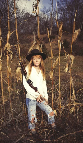 Молодая блондинка с пистолетом и стоящая на кукурузном поле — стоковое фото