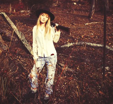 Ormanda bir silahla duran genç sarışın kadın