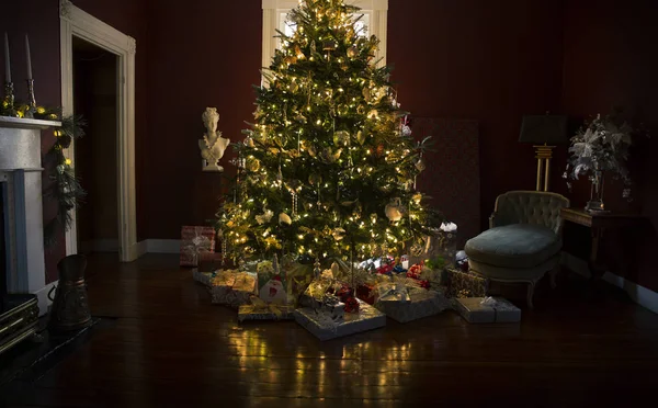 Weihnachtsbaum mit Geschenken und Lichtern, die sich auf dem Holzboden spiegeln — Stockfoto