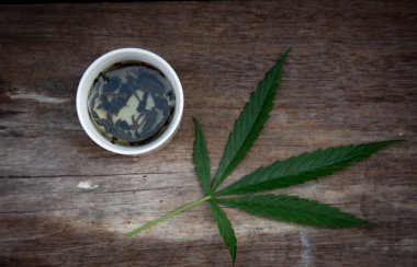 Eski ahşap bir masanın üzerine yeşil marihuana yaprakları ve marihuana çayı. Koyu ton. 