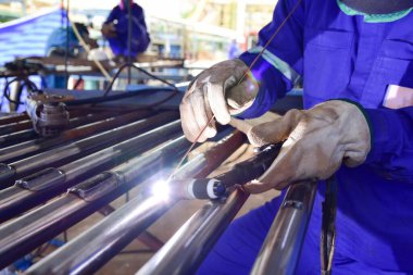 Kaynak makinesi boruya kaynak yapıyor. Tungsten Inert Gas Kaynak İşlemi (TIG). Kaynakçı koruyucu bir maske ve ısıya dayanıklı eldivenler takıyor.