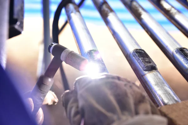The welder is welding the plate to the pipe with Tungsten Inert Gas Welding process (TIG). The welder wears protective equipment with a mask and heat resistant gloves