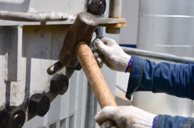 İşçiler büyük bir çekiç kullanarak somunu gevşetmek için İngiliz anahtarı kullanırlar. Metal rögar kapağını açmak için. Rögar kapağı başımızın üstünde..