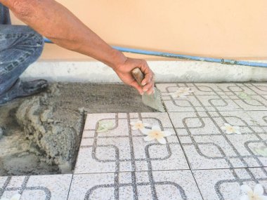 İşçinin eli yere çentikli malayla fayanslar yapıştırıyor.