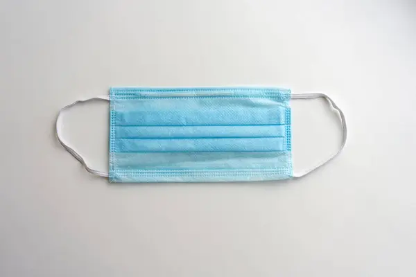 Mavi koruyucu tıbbi maske, beyaz arka planda, üst görünümde.