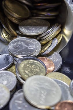 Eski bozuk paraların yıpranmış kenarları teneke bardaktan dökülüyor.
