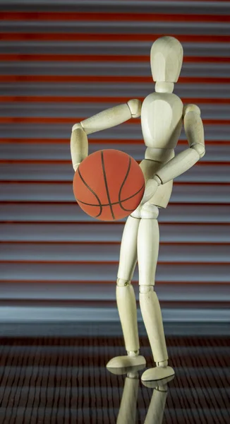 Wooden dummy with basketball in front of a jalousie plays with the ball