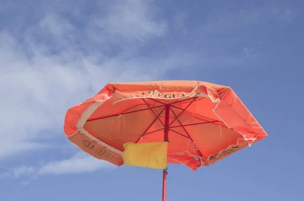 An orange umbrella with a yellow flag of lifeguard — Stock Photo, Image