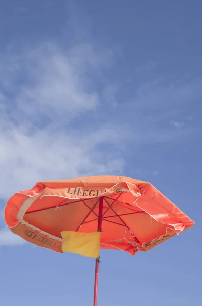 An orange umbrella with a yellow flag of lifeguard — Stock Photo, Image