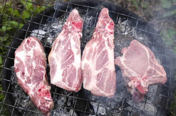 Quatro bifes de porco crus de churrasco com carvão vegetal — Fotografia de Stock