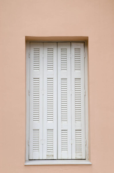Window with white wooden shutters on pink wall in Greece, Europ
