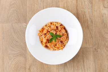 Fusilli, fesleğen yapraklı karides makarna ve ahşap arka planda beyaz bir tabakta parmesan peyniri.