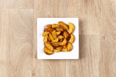 Tahta arka planda beyaz kare bir tabakta patates parçaları.