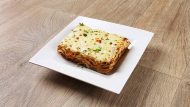 Klasik lazanya bolonez porsiyonu ahşap masa arkasında beyaz bir tabakta servis edilir.
