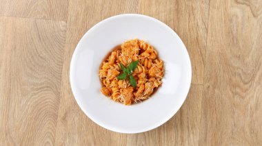 Fesleğen yapraklı kremalı tavuk fusilli makarna tarifi ve ahşap arka planda beyaz tabakta parmesan peyniri.