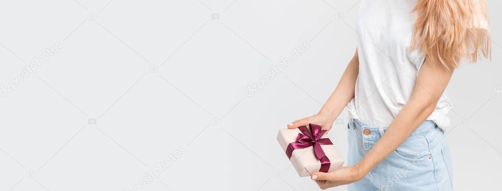 Close up studio portrait of caucasian girl in white t-shirt and jeans who holds in hands gift box with purple ribbon. Present for a birthday. Preparing for Christmas. Holidays concept. Copy space.