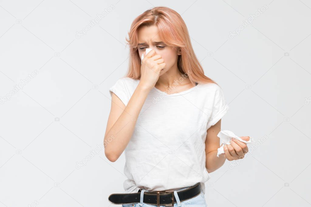 Studio portrait of young blonde woman blowing her nose into a paper napkin. The epidemic of cold, sneezing, allergy symptoms, flu, rhinitis, sickness, desperately sick. Healthcare and medicine concept