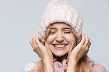 Pembe süveter ve beyaz şapkalı, sıradan / güzel bir kadın gibi giyinmiş, hoş bir iltifat aldıktan sonra olumlu duygular besleyen çekici bir kızın stüdyo portresini kapat..