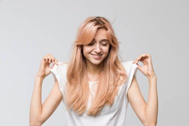 Beyaz tişörtlü güzel bir öğrencinin stüdyo portresi. Alçak bir görünüm ve çekici bir gülümseme. Elbiselerini esnet..