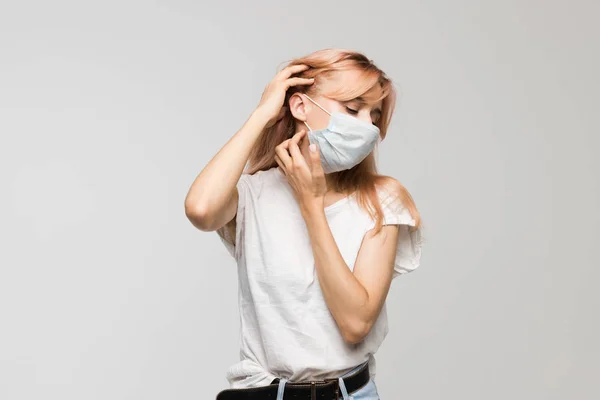Isolated studio portrait of young beautiful woman with medical mask in white shirt scratching neck/irritation, sensitive skin, allergy symptoms, rhinitis, cold, itch, healthcare and medicine concept.