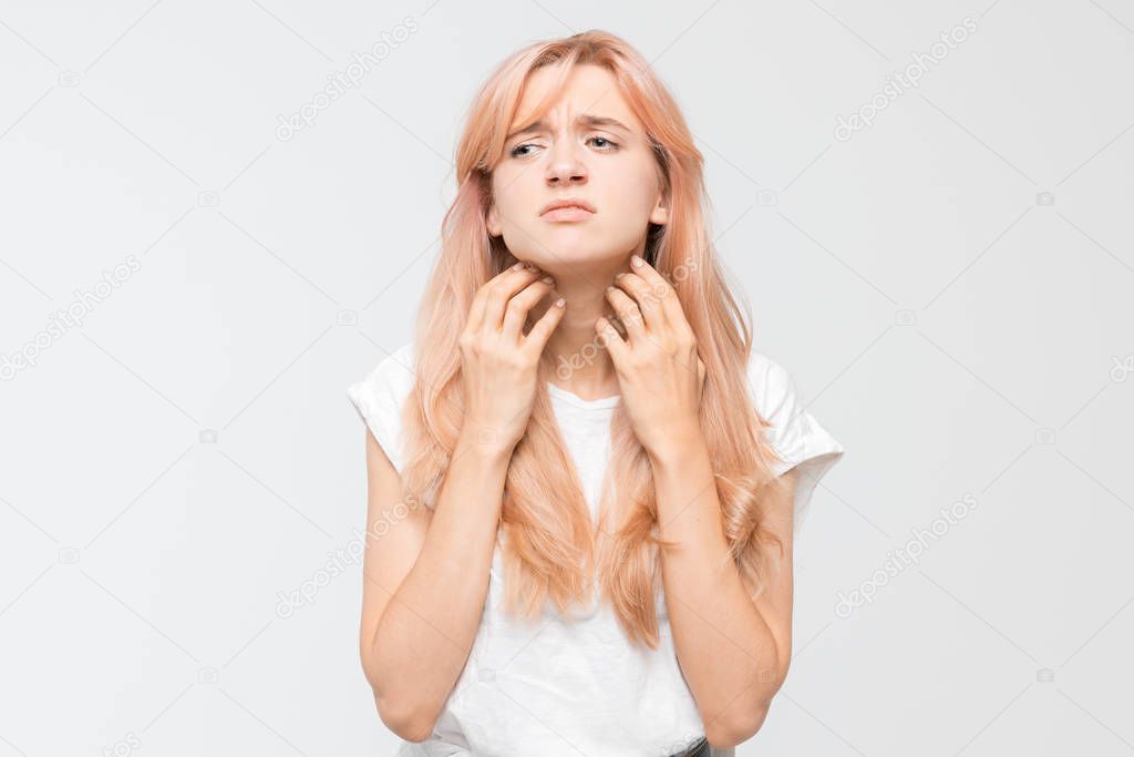 Portrait of young woman in white t-shirt who scratching itchy neck both hands. Itching causes the girl discomfort. Irritation, sensitive skin, allergy, dermatitis, insect bites. Healthcare concept.