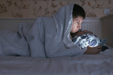 Uykulu adam akıllı telefon tutuyor ve uyumadan önce internette sörf yapıyor. Sosyal medya bağımlılığı, uyku bozukluğu, cep telefonuna bağımlılık, internet tuzağı. Uykusuzluk, uykusuzluk ve sağlık hizmetleri kavramında.