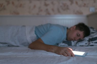 Adam elinde akıllı telefonuyla uyuyakalmış. Erkek cep telefonunu çok kullanır ve uyku bozukluklarından muzdariptir. Sosyal medya ve internet bağımlılığı. Sağlık hizmeti konsepti. Telefona seçici odaklanma.