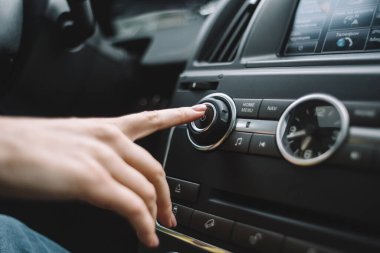 Multimedya sistemini çalıştırmak için uzanan bir kadının fotoğrafını kapat. Seçici odaklanma. Otomatikte müzik dinlemek. Güç düğmesi. Çevirisi: telefon, yolda navigasyon.