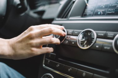 Multimedya sisteminin sesini açmak için uzanan bir kadının fotoğrafını kapat. Seçici odaklanma. Otomatikte müzik dinlemek. Çevirisi: telefon, yolda navigasyon.