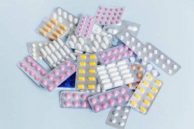 Farklı ilaçlar: beyaz, pembe ve sarı ilaç hapları, grip ilacı, baş ağrısı hapları, antibiyotikler. Tıbbi ve sağlık hizmetleri konsepti. Yumuşak odak, mavi arkaplan.