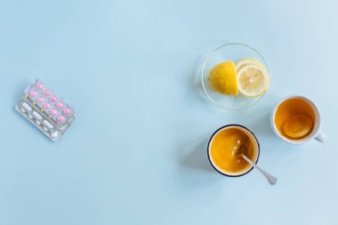 Sağ tarafta çay fincanı, bir fincan limon ve bal. Sol tarafta farklı ilaç hapları var. Tedavi metodu seçimi. Tıbbi ve sağlık hizmetleri konsepti. Düz konum, kopyalama alanı. Mavi arkaplan.