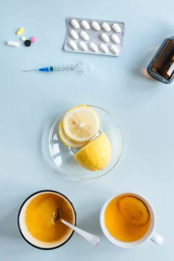 Evde tedavi, ilaçlara karşı. Bir fincan çay, bir fincan limon ve bal. Soğuk algınlığı ilaçlarının tedavisi. Düz yerde, üst tarafta. Dikey fotoğraf.