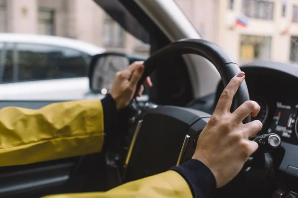 一个无法辨认的女孩的近照 她用双手开车 旅行的概念 有选择地专注于右臂 黄色的夹克模糊的背景 坐汽车旅行 舒适的交通 — 图库照片