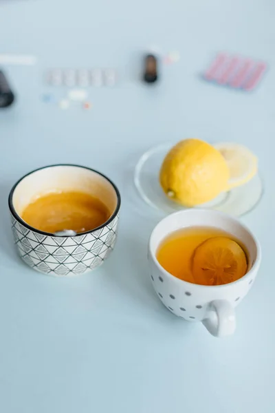 Bir fincan çay, bir fincan limon ve bal. Soğuk algınlığı ilaçlarının tedavisi. Seçici bir odak, arka plan, çeşitli haplar, grip ve burnun akması için bir tedavi. Sıcaklık bakımı kavramı.