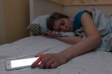 Güzel, bitkin kız elinde telefonla uyuyakalmış. Telefona odaklan. Beyaz perde. Yorgunluk, yorgunluk, aşırı çalışma. Sosyal ağlara bağımlılık, İnternet bağımlılığı, aşırı kullanım kavramı.