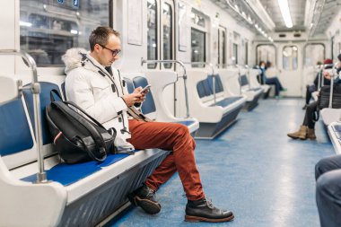 Metro treninde siyah sırt çantalı, gözlüklü yakışıklı bir yetişkin. Erkeğin elinde akıllı telefon var. Sosyal medya onu yuttu ve durağını kaçırdı. İnternet bağımlılığı. Boşluğu kopyala.
