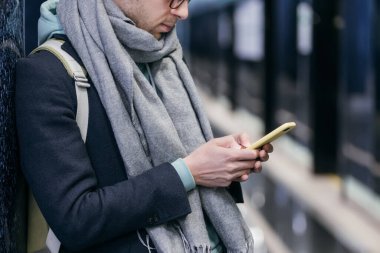 Genç hipster 'ın akıllı telefonuyla sohbet ettiği ve mesajlar gönderdiği ve tüm trenleri kaçırdığı kesilmiş bir fotoğraf. Sosyal ağlar gecikiyor ve çok zaman alıyor. Cep telefonu ve internet bağımlılığı kavramı