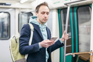 Genç adam metro trenine biniyor, tırabzan tutuyor ve cep telefonuna bakıyor, sohbet ediyor ve mesajlar gönderiyor, internette sörf yapıyor. Yaklaş, seçici odaklanma. İnsanlar ve iletişim konsepti.